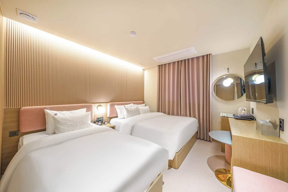 A hotel room with two beds, a desk, a mirror, and a television.