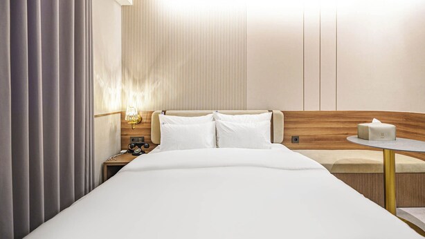 Habitación de hotel con cama, mesita de noche, lámpara y una pequeña mesa redonda con un dispensador de pañuelos.