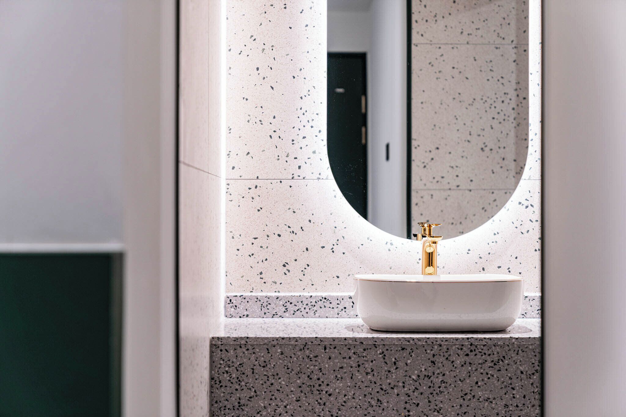 A bathroom with a white sink, gold faucet, and a speckled backsplash.
