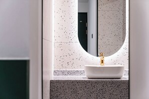 Une salle de bain avec un lavabo blanc, un robinet doré et un pare-éclaboussures à motifs.