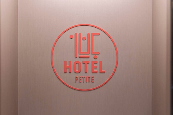 Un logo circulaire avec les mots « HÔTEL PETITE » sur un mur à texture.