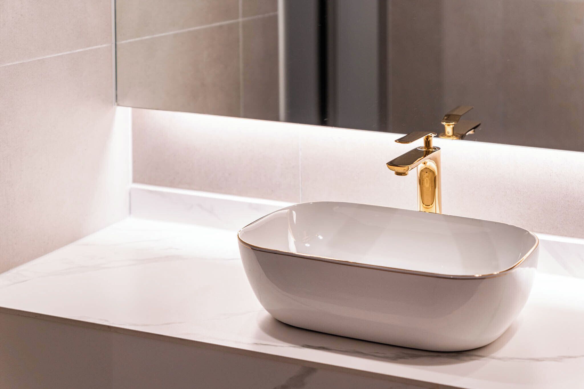 A bathroom with a white marble sink, gold faucet, and a mirror above it.