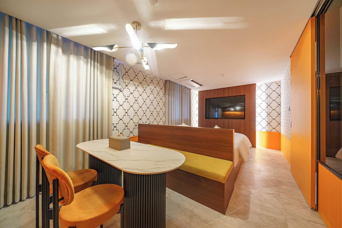 A modern hotel room with a dining area, a sofa, a television, and patterned walls.