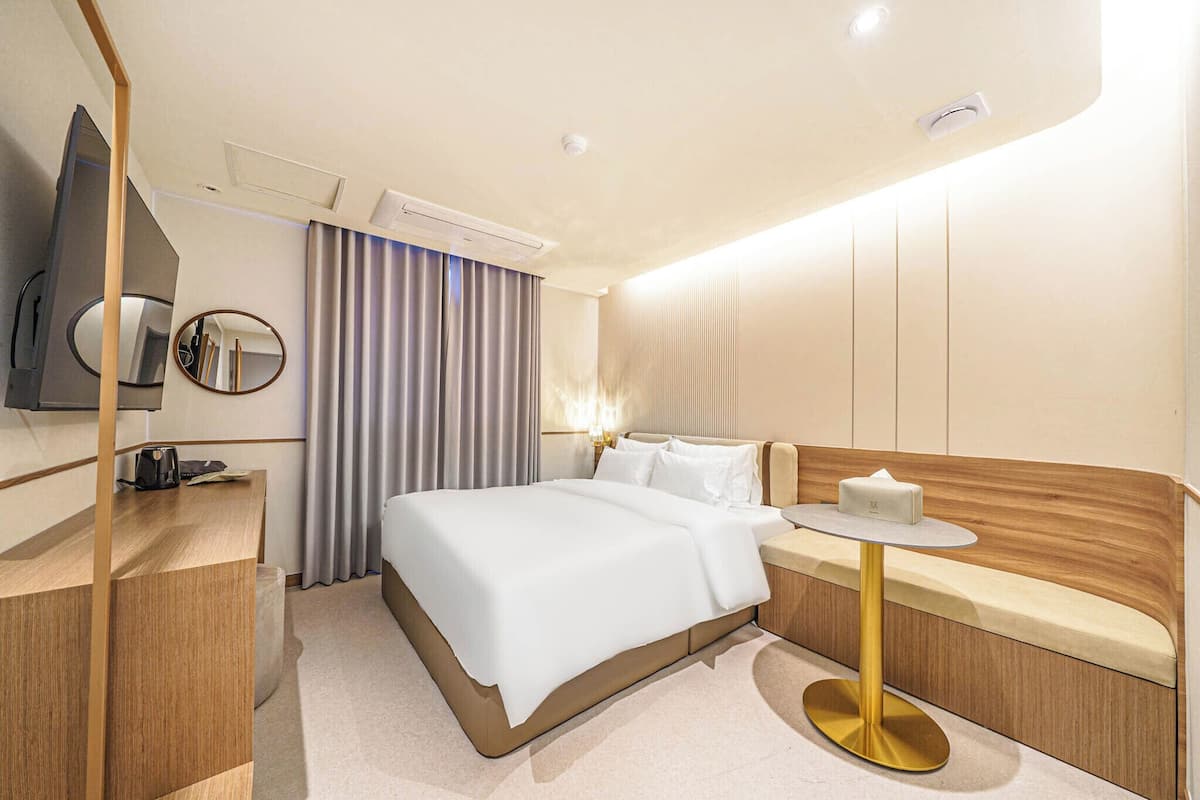 A hotel room with a bed, bedside table, mirror, and a TV.