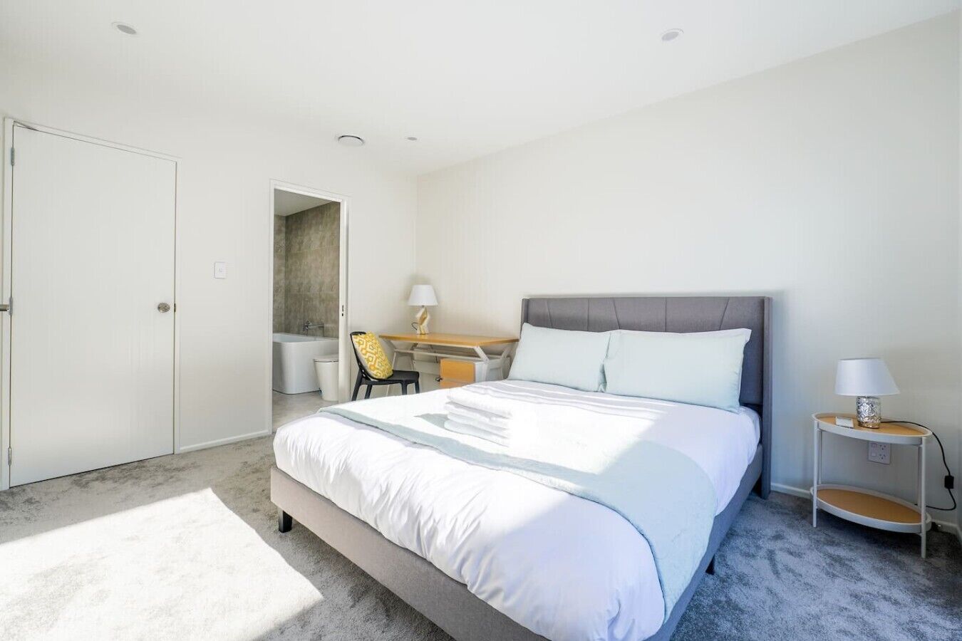 Ein modernes Hotelzimmer mit einem großen Bett, einem Schreibtisch, einem Sessel und einem kleinen Nachttisch.