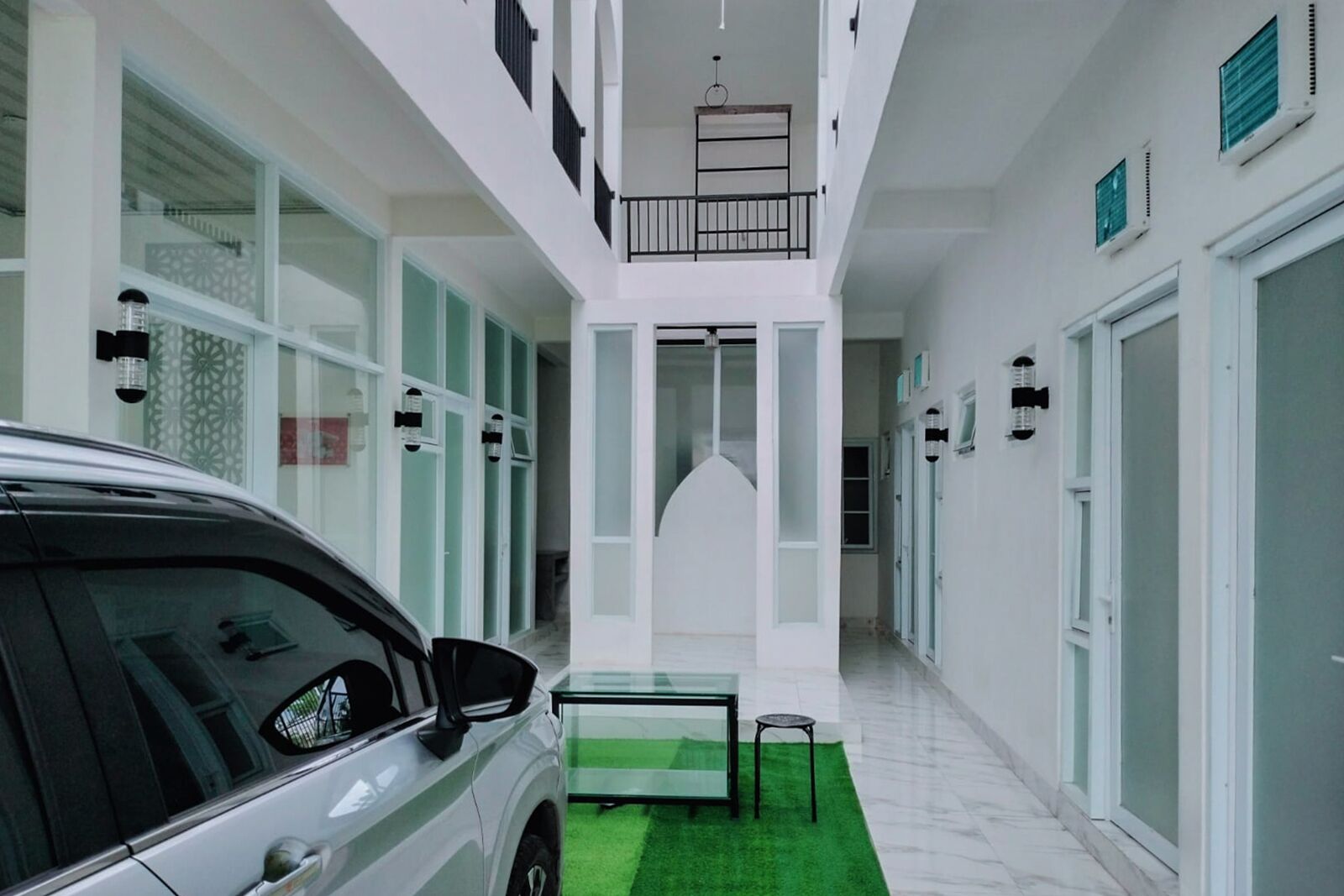 A modern building with a car parked outside, a green artificial grass area, and a balcony with a railing.