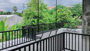 A balcony with a metal railing, a concrete wall, and a view of a street with trees and buildings in the background. - TwoSpaces at Arfina Residence Syariah, Lamongan (Paciran)