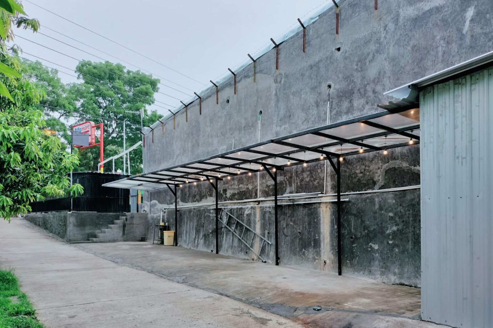 A covered outdoor area with a concrete wall and metal beams, a staircase, and a metal door.