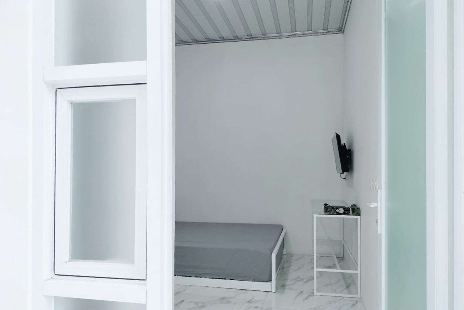 Un dormitorio con una cama, un estante pequeño y un televisor montado en la pared.