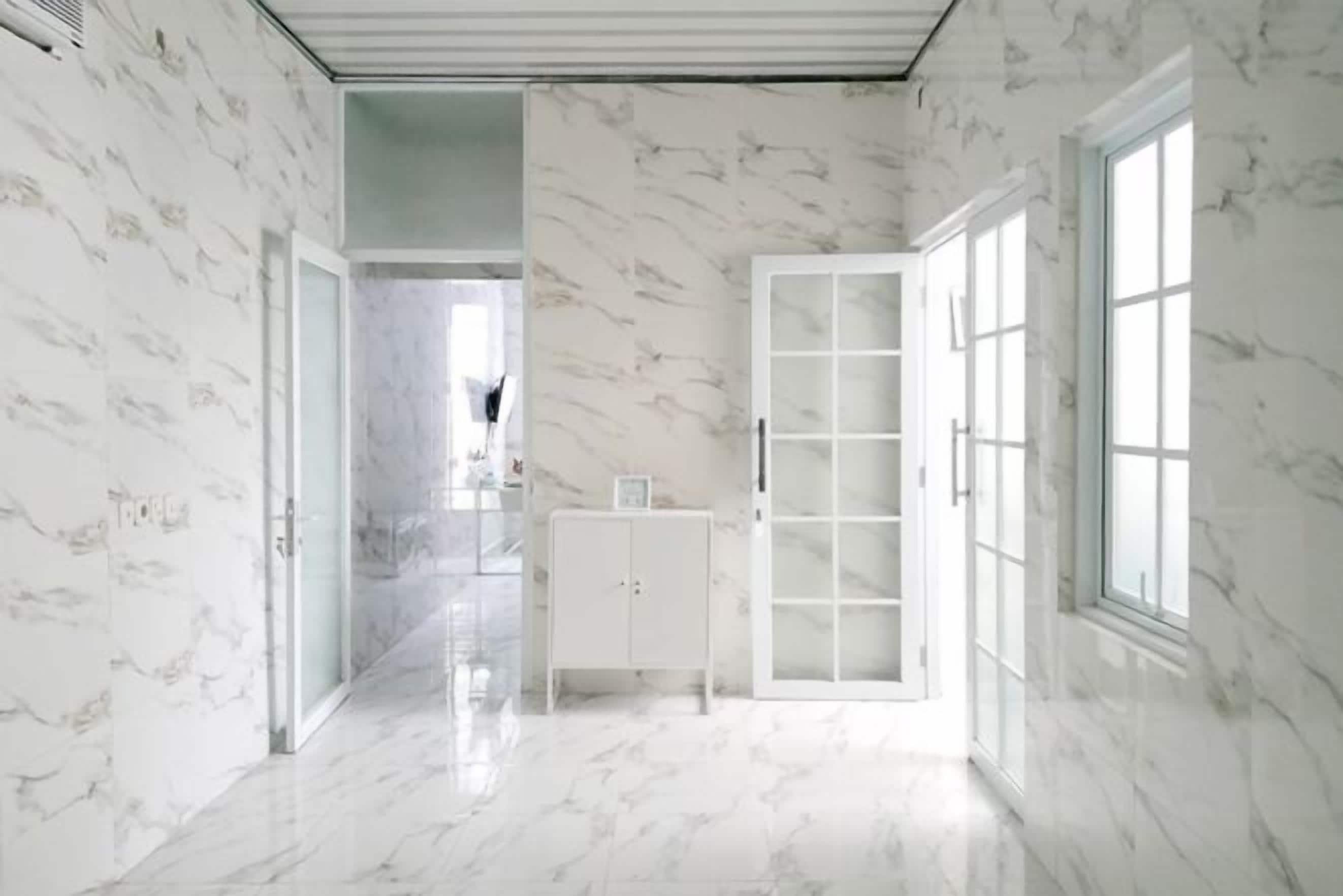 Um corredor com paredes e pisos de mármore, que leva a um quarto com uma grande janela e um armário branco.