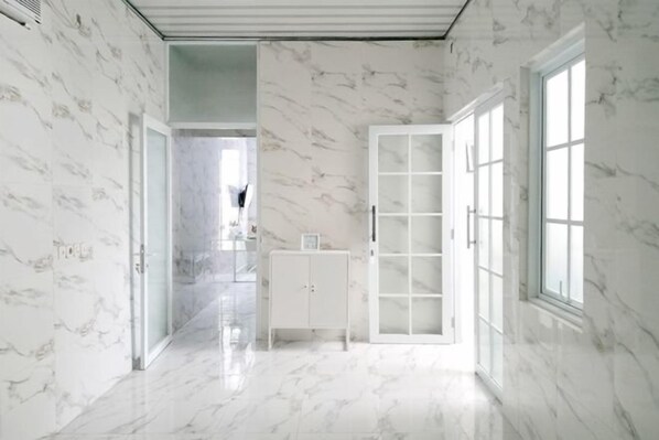 A hallway with marble walls and floors, leading to a room with a large window and a white cabinet. - TwoSpaces at Arfina Residence Syariah, Lamongan (Paciran)