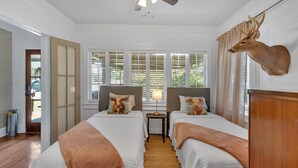 Ein Schlafzimmer mit zwei Betten, einem Deckenventilator, einem aufgehängten Hirschgeweih und Blick ins Grüne durch die Fenster.