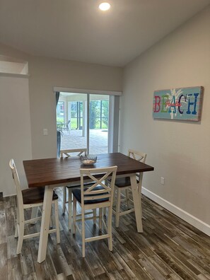 A dining area with a wooden table and white chairs, a glass bowl on the table, and a 'Beach Paradise' sign on the wall.