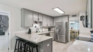Una cocina moderna con armarios grises, electrodomésticos de acero inoxidable y una isla de mármol con taburetes.