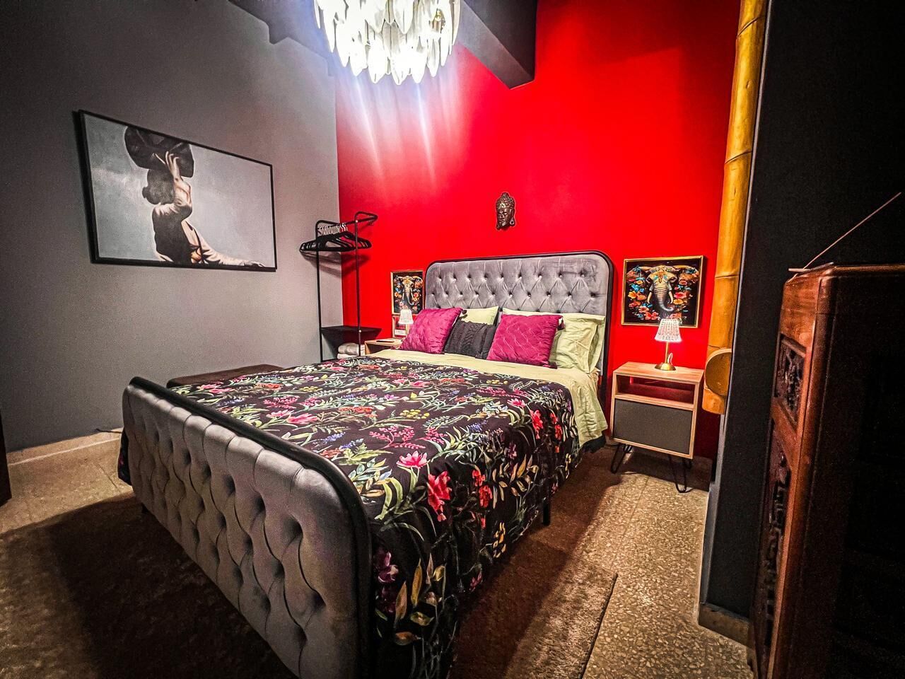A bedroom with a tufted headboard, a floral bedspread, and a red accent wall.