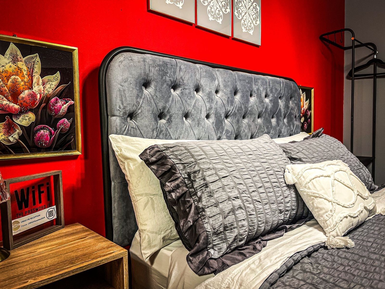 Une chambre avec une tête de lit capitonnée, plusieurs oreillers, une œuvre d’art encadrée et un panneau indiquant la disponibilité du Wi-Fi.