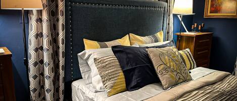 A neatly made bed with a dark headboard, multiple pillows, and a bedside table with a lamp.