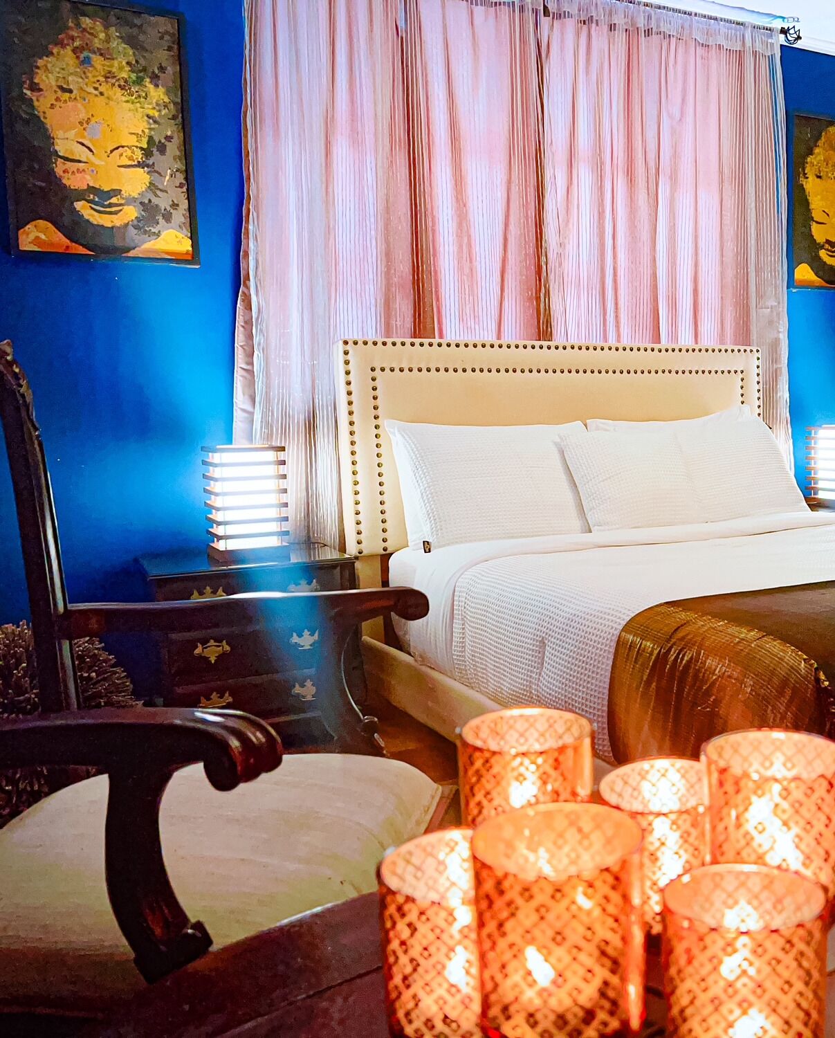 Un dormitorio con una cama, una mesita de noche, una silla y lámparas decorativas.