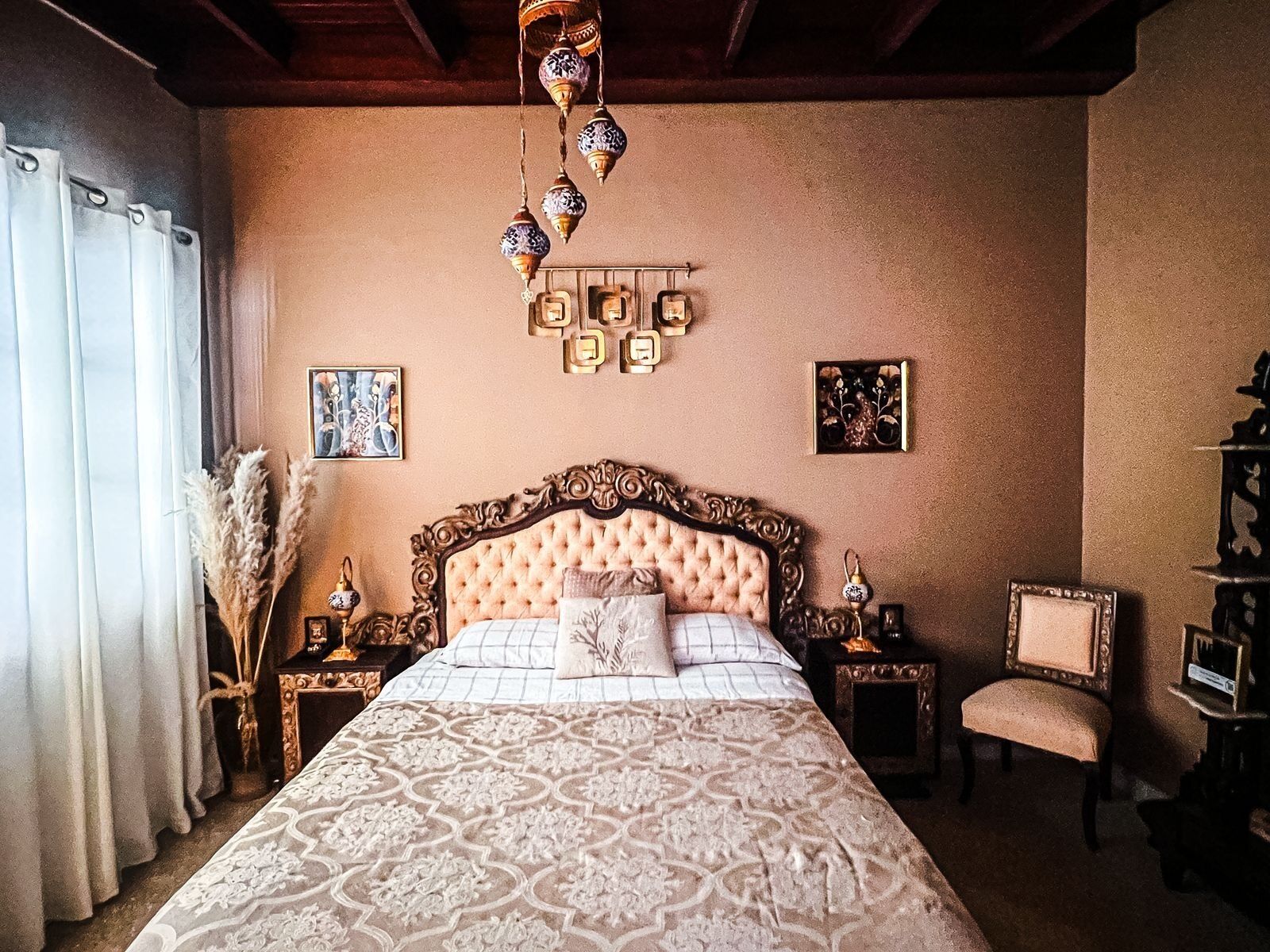 A bedroom with a large bed, ornate headboard, decorative wall sconces, and a classic chair.