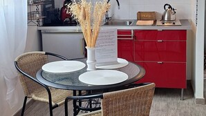 A compact kitchen with red cabinets, a microwave, and a kettle. There is a dining table with two chairs and a menu stand.