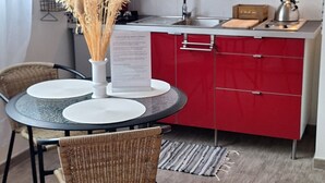 A compact kitchen with red cabinets, a white microwave, and a small dining area with wicker chairs and a round table.