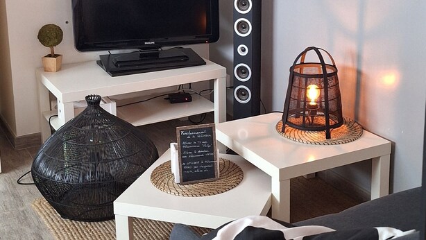 A modern living room with a flat-screen TV, a white coffee table, a black pouf, a black sofa, and decorative wall art.