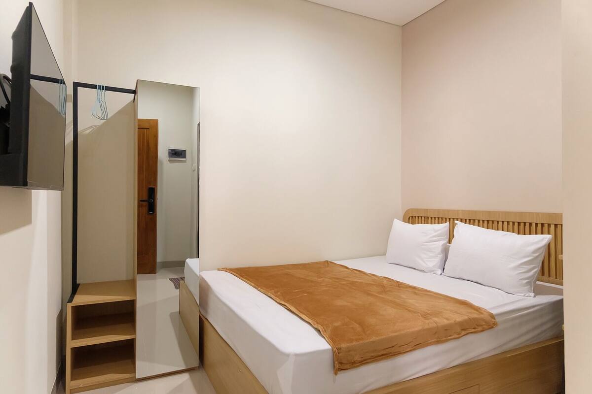 A bedroom with a bed, a wooden headboard, a brown blanket, and a TV mounted on the wall.