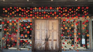 A storefront with a wooden door and large windows, decorated with hanging paper flowers.