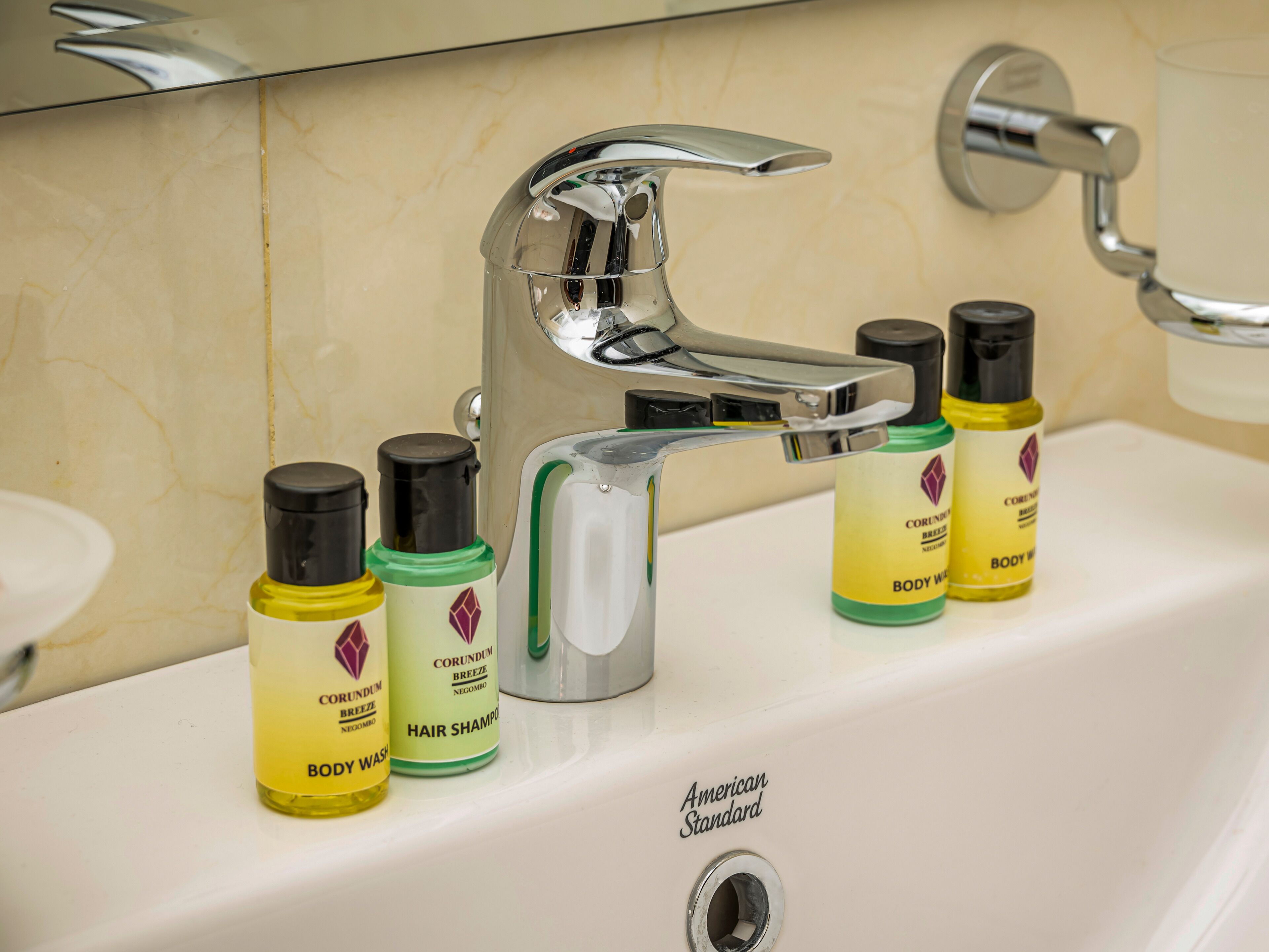 A bathroom sink with a chrome faucet and three bottles of Corundum body wash and hair shampoo.