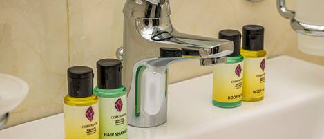 A bathroom sink with a chrome faucet and three bottles of Corundum body wash and hair shampoo.