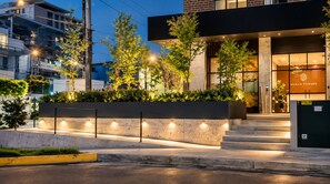 A modern building with a staircase leading to the entrance, surrounded by greenery and illuminated by street lighting.