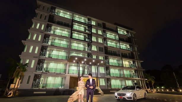Un hotel de varios pisos con ventanas e balcones iluminados, un coche blanco estacionado adelante y una palmera cerca.