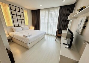 Ein modernes Hotelzimmer mit einem großen Bett, einem Schreibtisch mit Computer und einem großen Fenster mit Vorhängen.