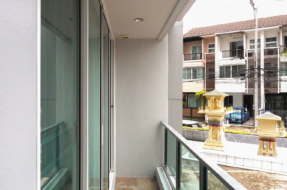 A balcony with a glass railing overlooking a courtyard with a fountain and a building in the background.