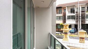 A balcony with a glass railing overlooking a courtyard with a fountain and a building in the background.