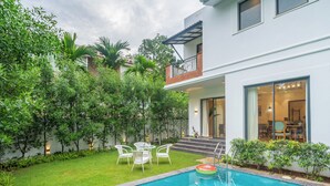 A modern house with a swimming pool, a patio with chairs, and a well-maintained garden.