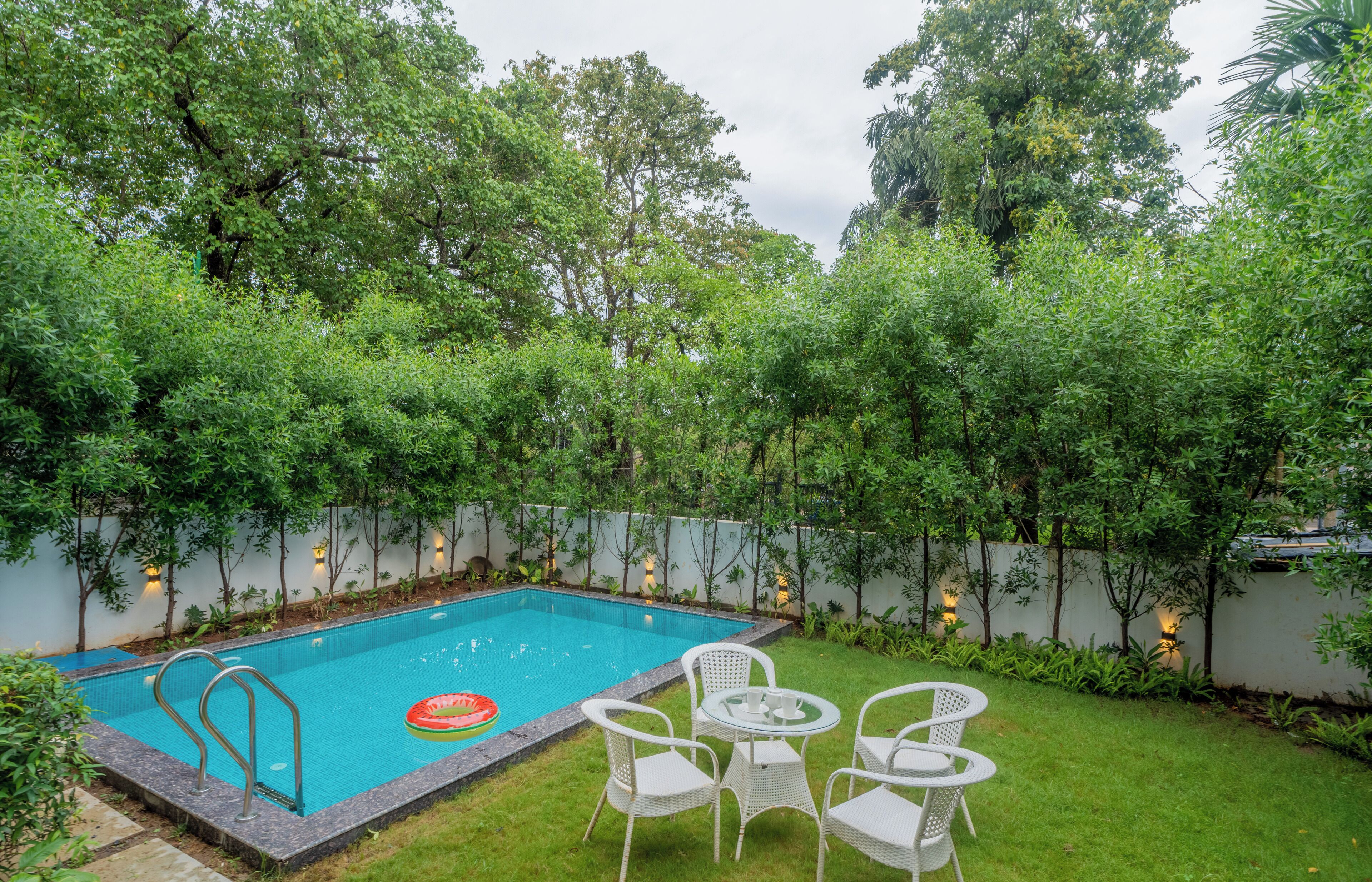 Une piscine rectangulaire avec un escalier, entourée de chaises blanches et d’une table.