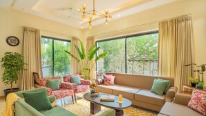 A spacious living room with a sofa, armchairs, a coffee table, and large windows offering a view of greenery outside.