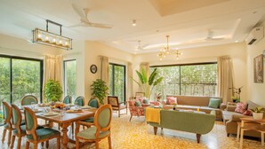 A spacious living area with a dining table, chairs, a sofa, and a large window offering a view of trees.