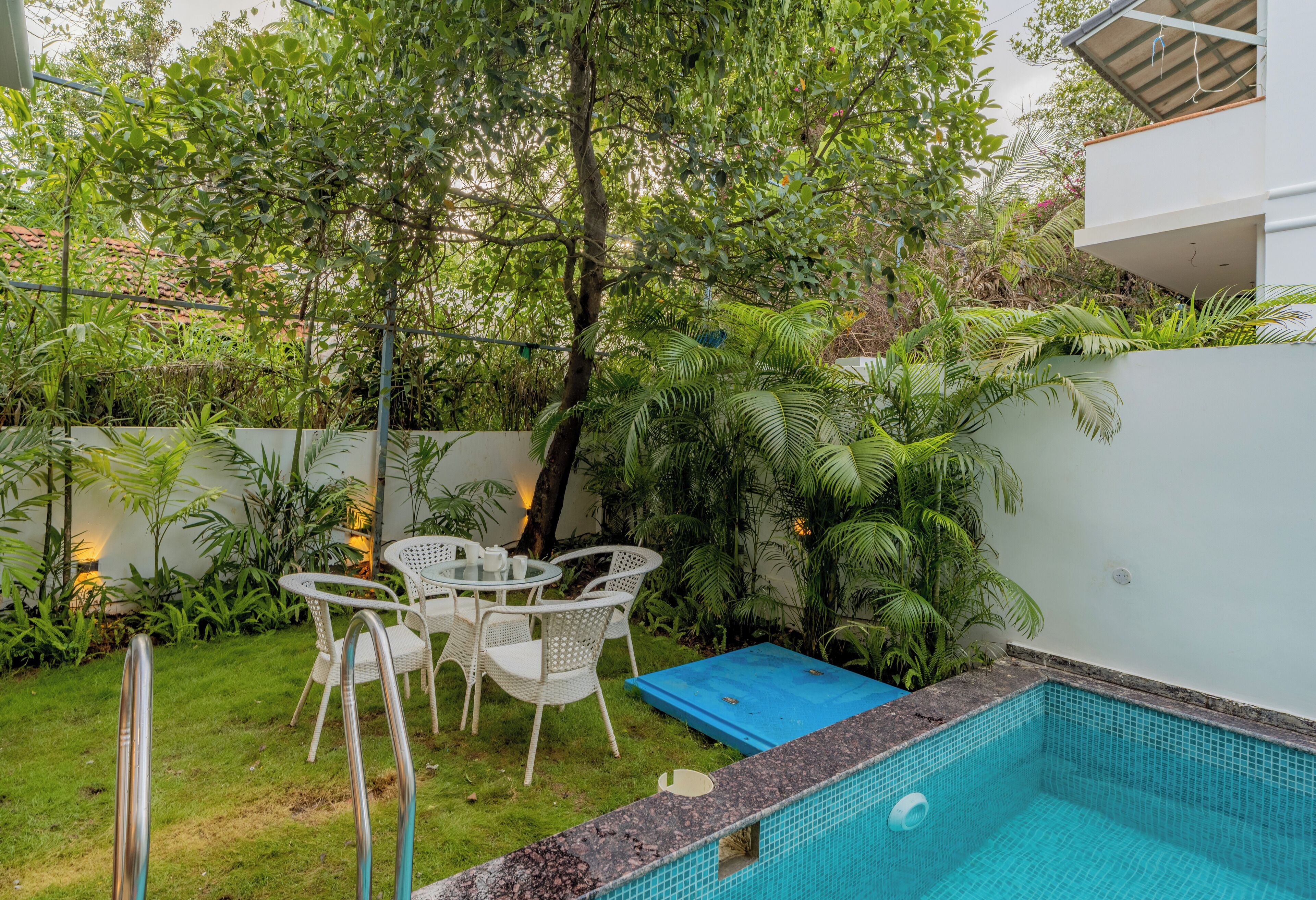 A backyard with a swimming pool, white outdoor furniture, and lush greenery.