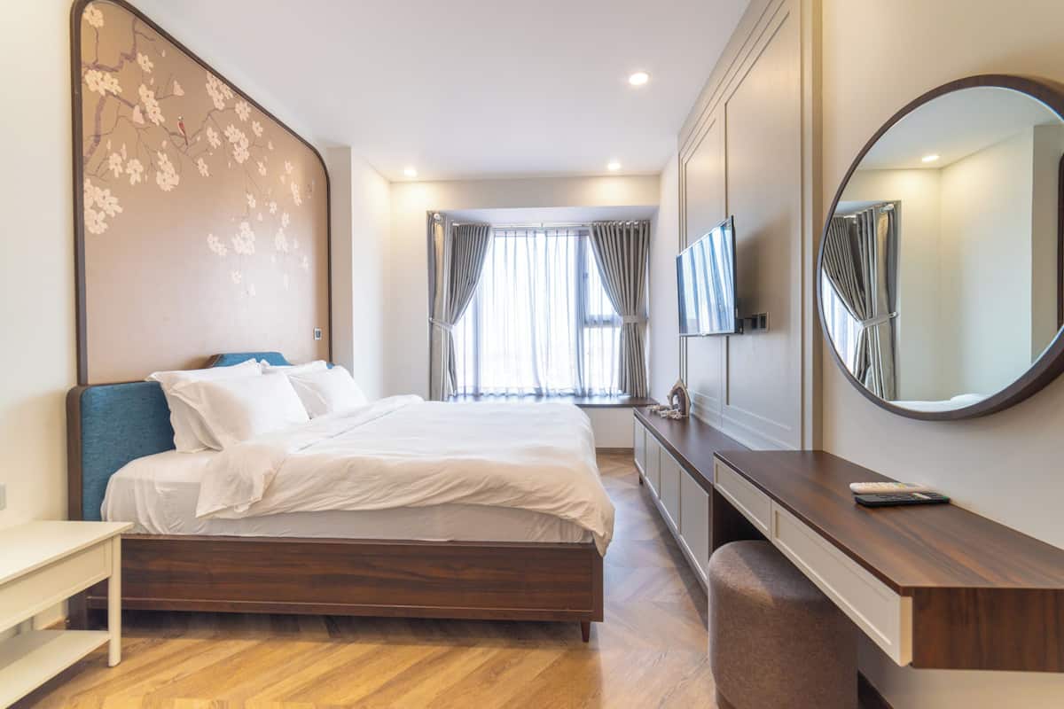 A modern bedroom with a wooden bed, a bedside table, a large mirror, and a window with curtains.
