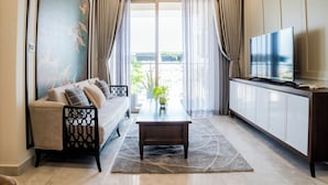 A living room with a sofa, a coffee table, a TV on a cabinet, and a view through a glass door. - Midtown Premium Apartments (Ho Chi Minh City)