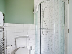A bathroom with a glass-enclosed shower, white tiled walls, and a toilet.