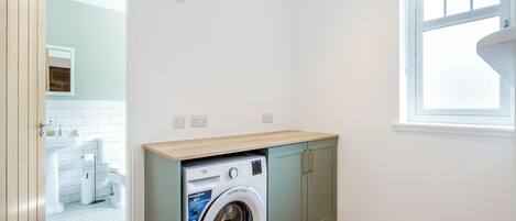 A laundry room with a washing machine, grey cabinets, and a window.