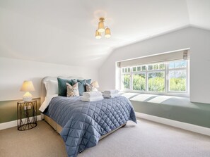 A bedroom with a bed, pillows, a bedside table with a lamp, a window with a view, and a ceiling light fixture.