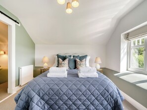 A bedroom with a large bed, two bedside lamps, a radiator, and a window with a view of greenery.