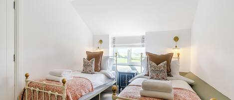 A bedroom with two beds, a window, and a ceiling light fixture.