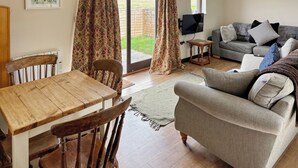 A living room with a sofa, a dining table, chairs, a TV, and a sliding glass door leading to an outdoor area.