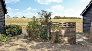A gravel driveway leading to a wooden gate with a field in the background.