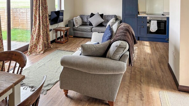 A living room with a sofa, a dining table, and a kitchen area with a built-in oven.